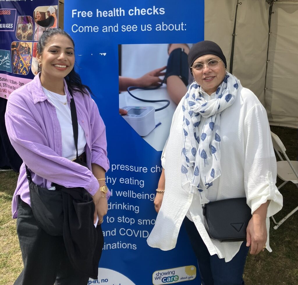 Local residents Fatimah and Shahida stand by the sign which reads: 'Free health checks. Come and see us about:'