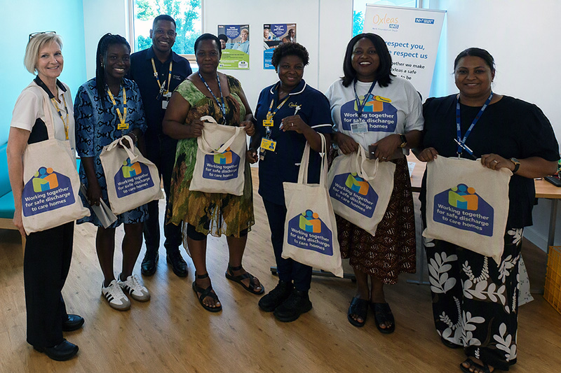 Hospital staff, care home staff and campaign participants stand together during a South East London ICS ward visit, holding tote bags promoting the “Working Together for Safer Discharge to Care Homes” campaign.