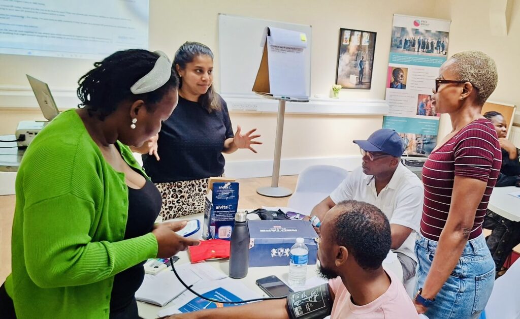A photo of a group of people talking and 1 person is getting their blood pressure checked