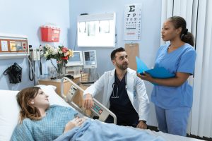 A woman in a hospital bed. Near to her, a male healthcare professional looks at his female colleague.